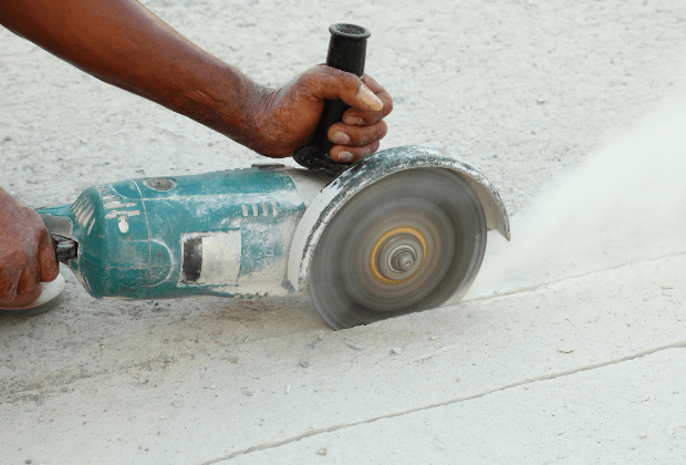 Contractor using a small hand saw to cut through a concrete sidewalk